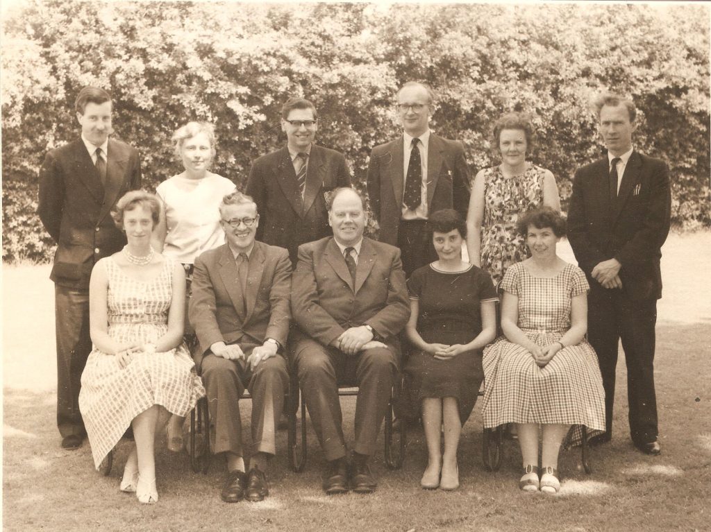 Group photograph of 5 men and 6 women. Five of them are on chairs, 6 are standing behind. The men are wearing suits and the women are in summer dresses.