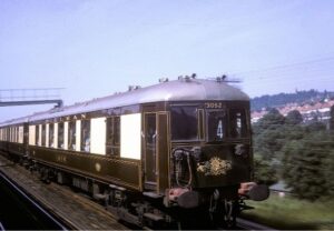 Brown and cream pullman carriages on track with countryside behind.