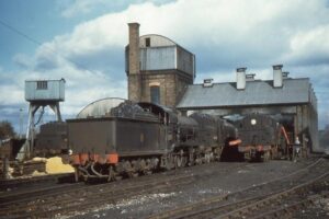 Brick locomotive sheds and tower. Locomotives on tracks in front of this.