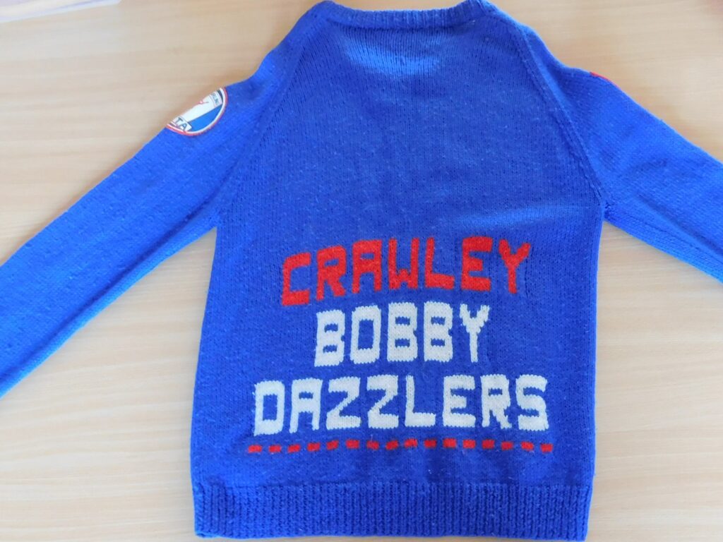 Blue knitted jumper with words 'Crawley Bobby Dazzlers' written on the front.