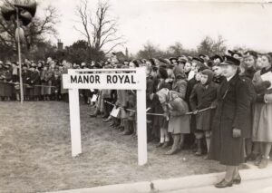 Black and white image of a group of people behind a sign saying Manor Royal