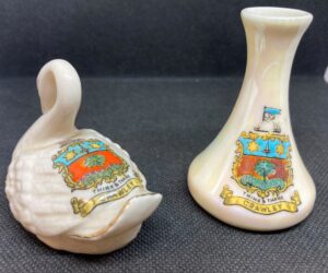 Two ceramic items with a coat of arms on the front on black background.