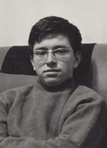 Black and white photo of a young man wearing glasses and a high neck jumper.