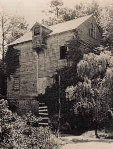 Black and white image of a derelict four story building surrounded by trees.