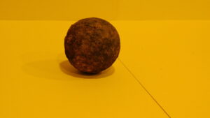 Rusted iron cannon ball on yellow background.