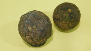 Two rusted iron balls, one slightly larger with wire around it, on yellow background.