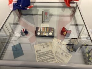 Glass display case with medals and documents inside.