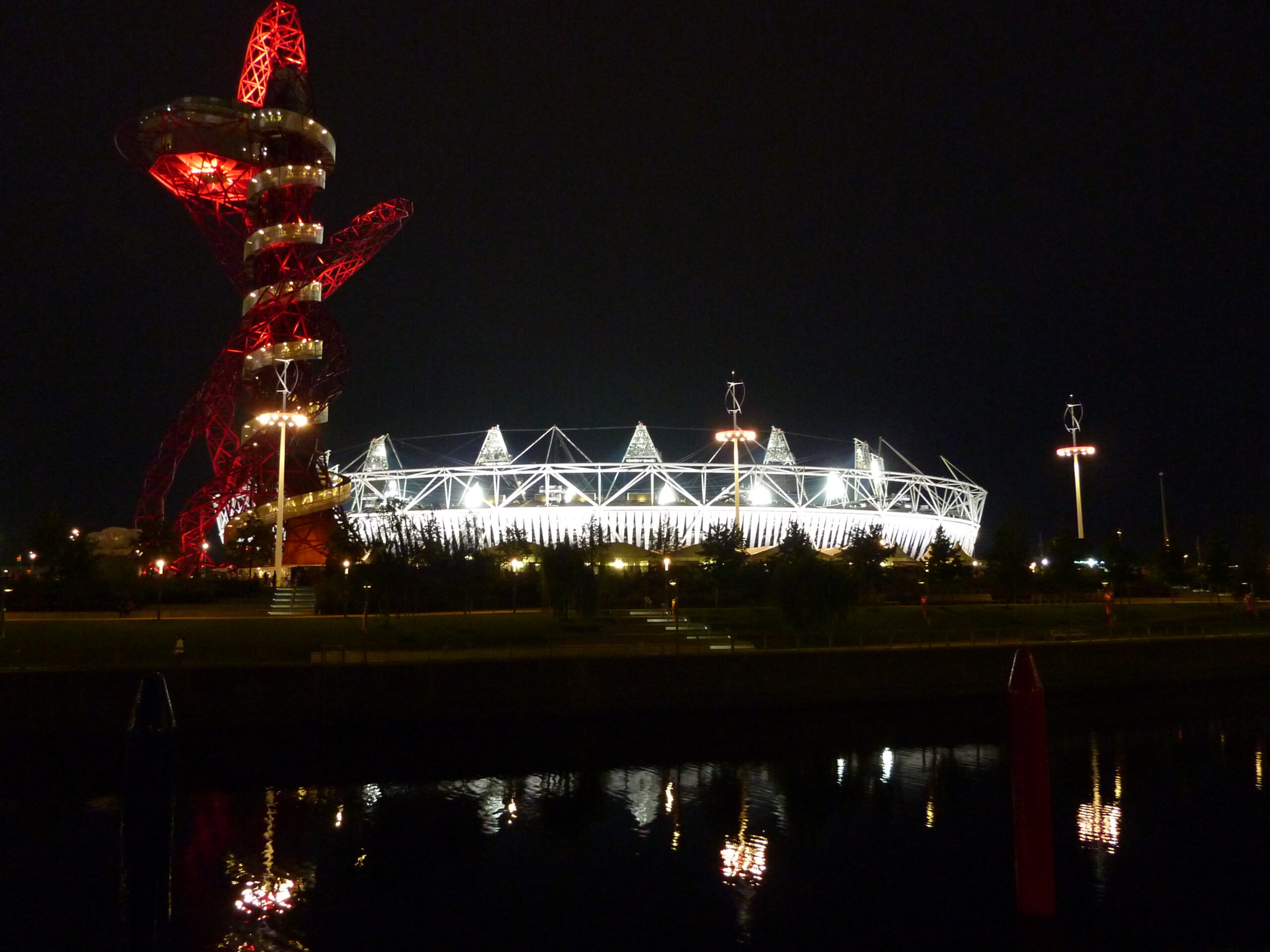 Night time photograph of Stadium lighten up in white, with another structure lit up in red on the left. 