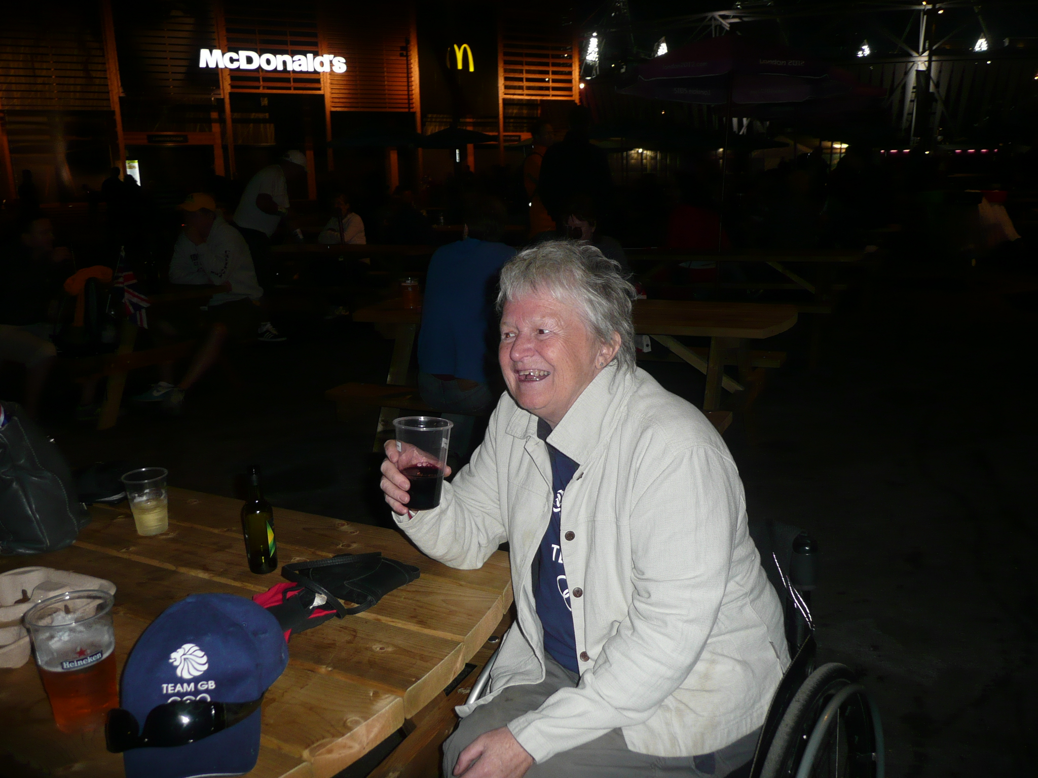 Colour image of a woman in a white top sitting at a table and holding a drink. 