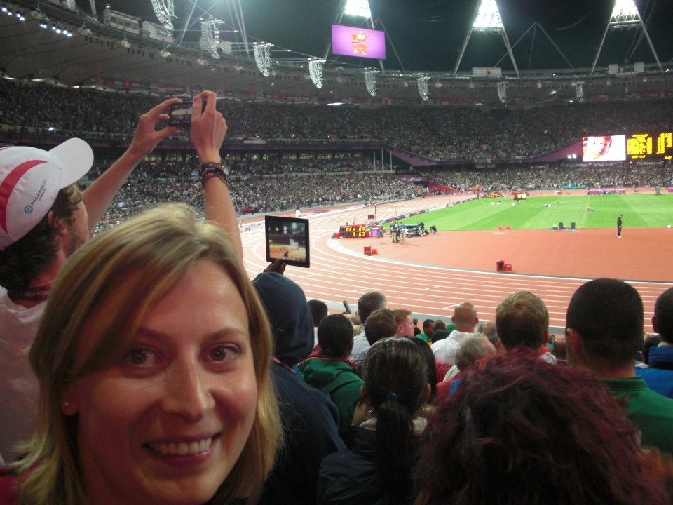 A woman looks at the camera with a stadium of people and running track behind her. 