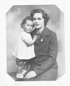  Black and white photograph of a woman in a dark jacket and small girl in a white dress. 