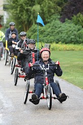 A line of wheel chairs moving through the park.