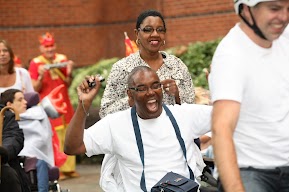 Man sitting down has his arms up in celebration. Other people are standing around him. 