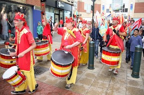 People in red outfits and drums, there are people behind them. 