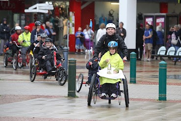 woman in wheel chairs comes across pavement with other wheel chairs behind her. 