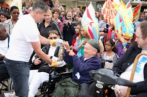 The flame in a gold lantern is held by members of the crowd. 