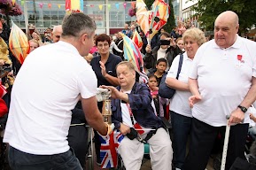 The flame in a gold lantern is held by members of the crowd. 