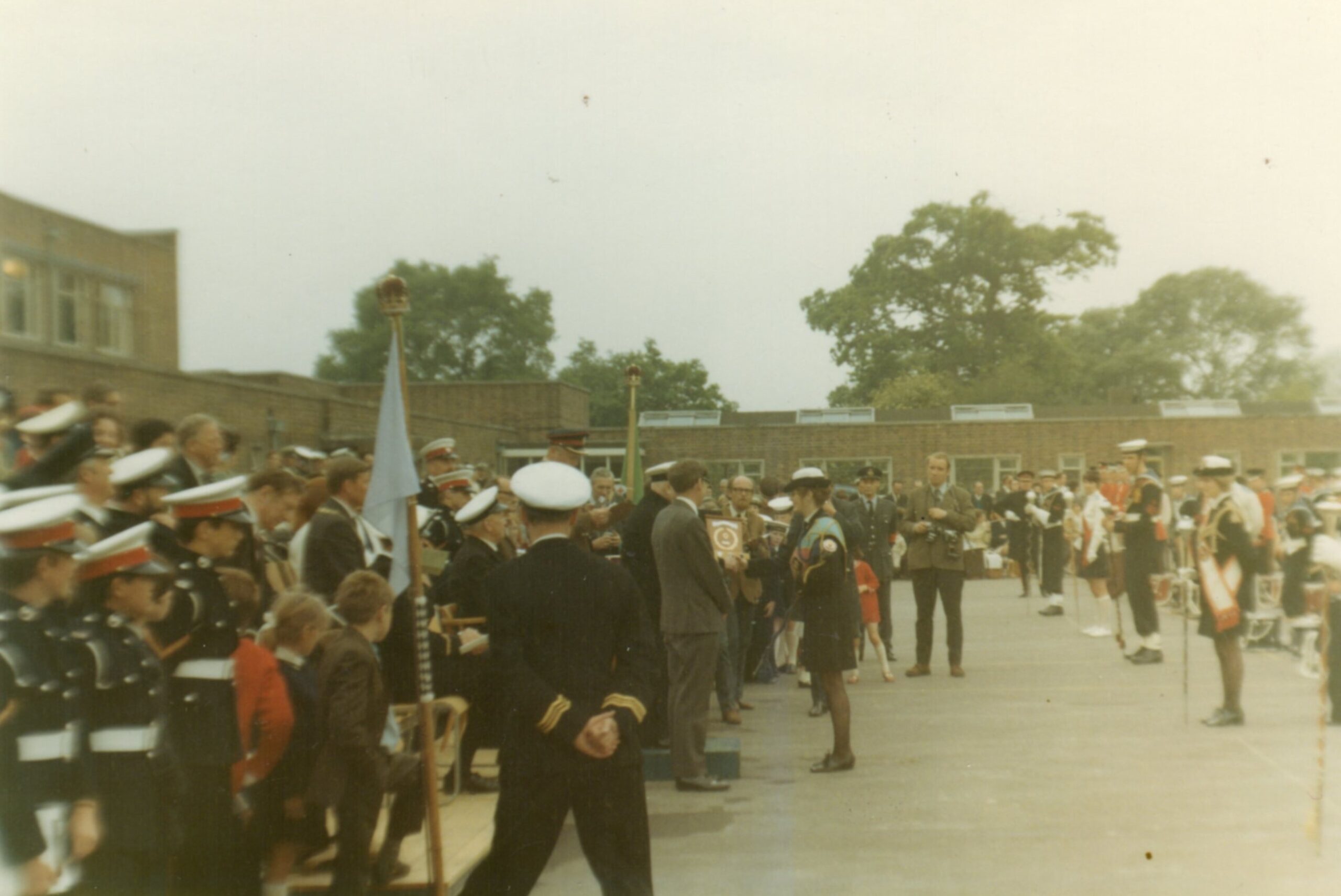 Colour photograph of a group of being in uniforms standing outside one woman in the middle is being presented with a trophy. 