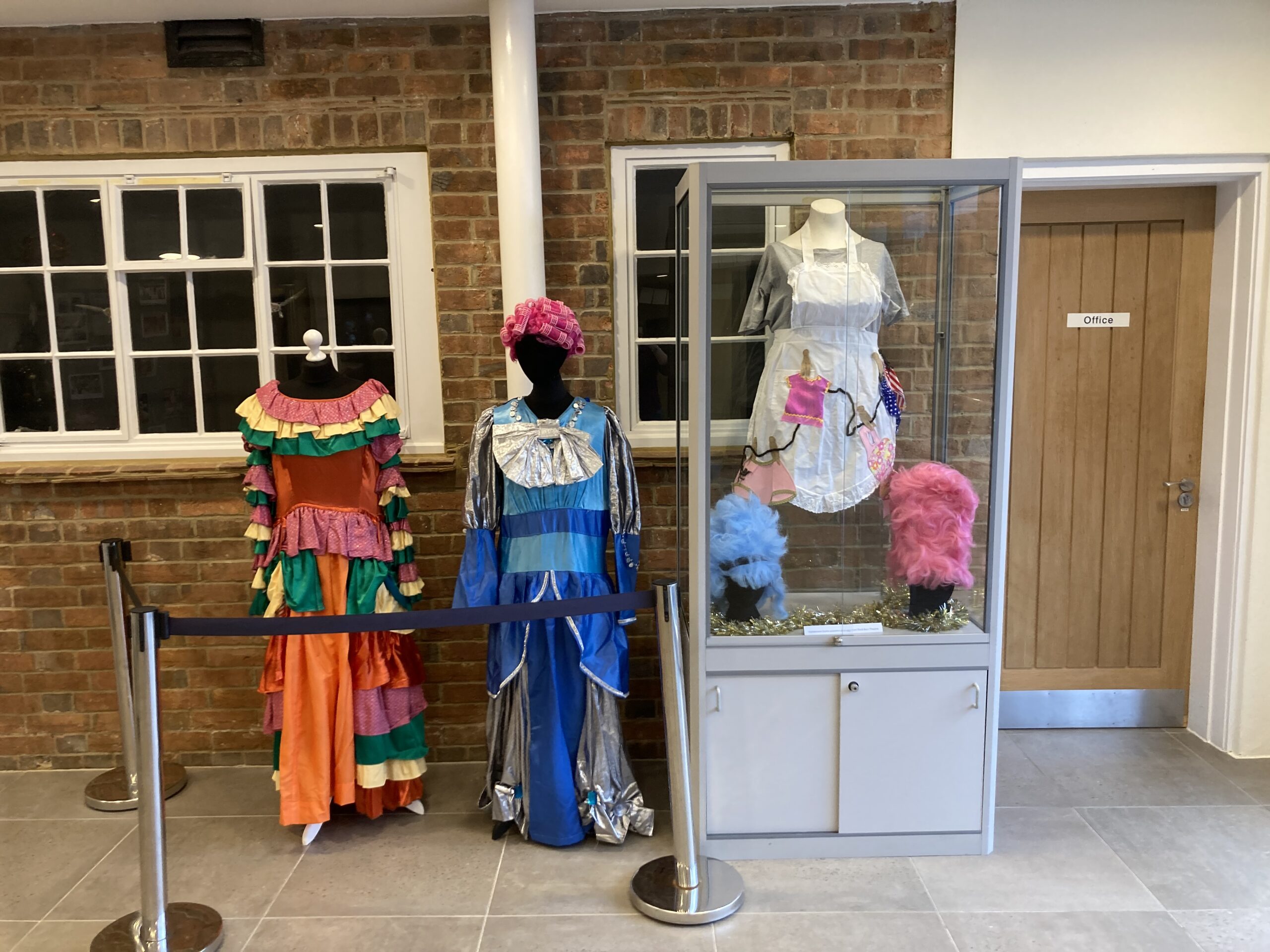 Two mannikins in colourful clothes on the left and display case with another manikin in on the right.